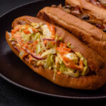 Hotdog with grilled sausage with cabbage, carrots and onions in a bun with salt, spices and herbs