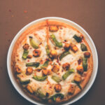 Paneer Pizza is an indian version of Italian dish topped with Cottage Cheese, served in a plate with white sauce. selective focus